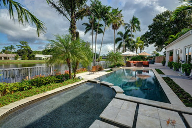 Example of a large island style backyard rectangular infinity hot tub design in Miami