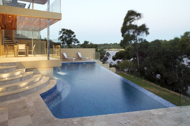 Diseño de piscina con fuente elevada minimalista a medida en patio trasero con adoquines de piedra natural