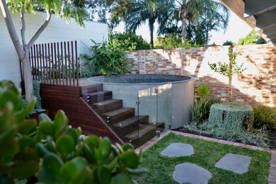 Ejemplo de piscina elevada moderna pequeña redondeada en patio trasero con paisajismo de piscina y adoquines de piedra natural