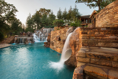 Design ideas for an expansive rustic back custom shaped natural swimming pool in Oklahoma City with a water slide and natural stone paving.