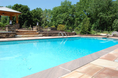Ejemplo de piscina alargada rural grande rectangular en patio trasero con adoquines de hormigón