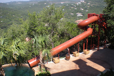 Immagine di una grande piscina naturale tropicale personalizzata dietro casa con un acquascivolo e lastre di cemento