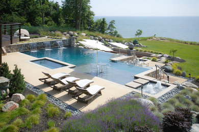 Foto di un'ampia piscina a sfioro infinito personalizzata dietro casa con fontane e pavimentazioni in pietra naturale