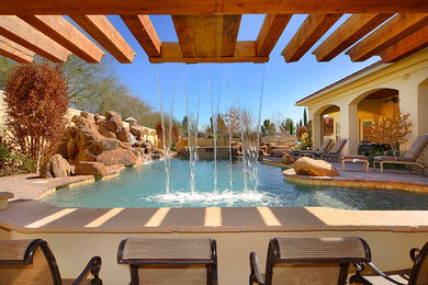 Medium sized rustic back custom shaped swimming pool in Phoenix with a water feature and natural stone paving.