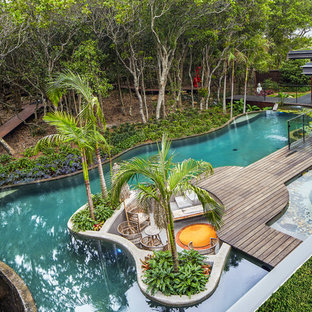 Inspiration for a tropical backyard custom-shaped infinity pool in Other with decking.