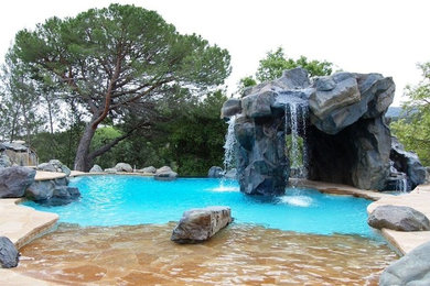 Cette image montre une grande piscine naturelle et arrière ethnique sur mesure avec un point d'eau et des pavés en pierre naturelle.