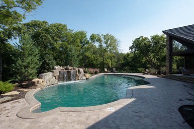 Example of a mid-sized mountain style backyard stamped concrete and custom-shaped natural pool design in Kansas City
