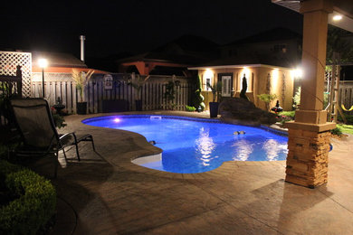 Imagen de piscina alargada tropical de tamaño medio tipo riñón en patio trasero con adoquines de ladrillo