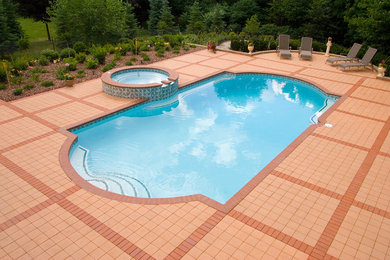 Modelo de piscinas y jacuzzis tradicionales de tamaño medio rectangulares en patio trasero con adoquines de ladrillo