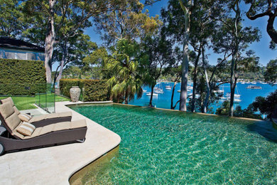 Modelo de piscina infinita moderna grande a medida en patio trasero con paisajismo de piscina y adoquines de piedra natural