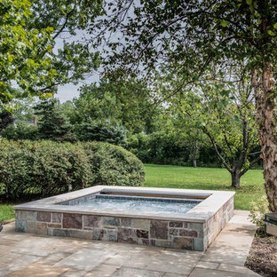 This is an example of a small country backyard rectangular natural pool in Chicago with a hot tub and natural stone pavers.