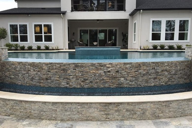 Diseño de piscina con fuente infinita contemporánea de tamaño medio rectangular en patio trasero con adoquines de piedra natural