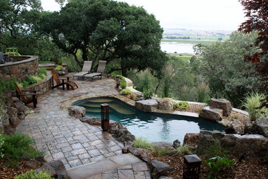 Ejemplo de piscina con fuente rural grande a medida en patio trasero con adoquines de hormigón