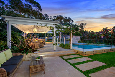 Ejemplo de casa de la piscina y piscina alargada actual de tamaño medio en forma de L en patio trasero con adoquines de piedra natural