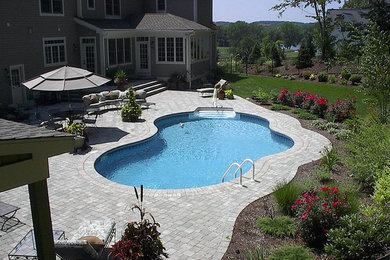 Imagen de piscina natural grande a medida en patio trasero con adoquines de hormigón