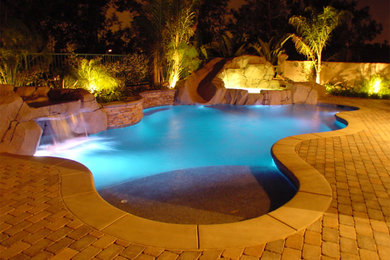 Diseño de piscina con tobogán de tamaño medio tipo riñón en patio trasero con adoquines de ladrillo