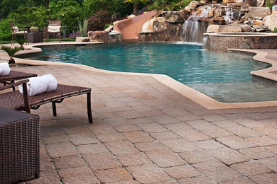 Diseño de piscina con tobogán grande a medida en patio trasero con adoquines de ladrillo