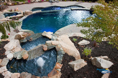 Imagen de piscina con fuente alargada clásica grande a medida en patio trasero con adoquines de piedra natural