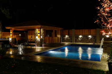 Ejemplo de piscina con fuente alargada clásica grande rectangular en patio trasero con adoquines de piedra natural