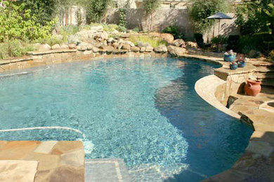 This is an example of a large traditional back custom shaped lengths swimming pool in Austin with a water feature and natural stone paving.