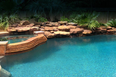 Exemple d'une grande piscine arrière exotique sur mesure avec un bain bouillonnant et des pavés en béton.