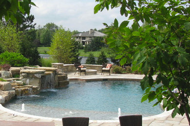Photo of a large modern back custom shaped natural swimming pool in Detroit with concrete paving and a water feature.