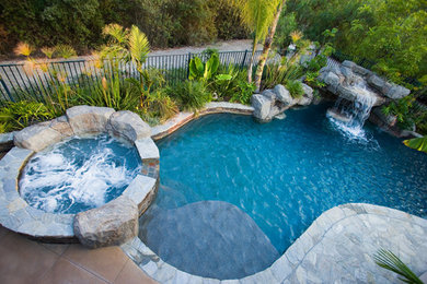 Inspiration for a tropical backyard stone and custom-shaped hot tub remodel in Orange County