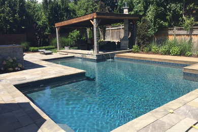 Modelo de piscina con fuente alargada clásica renovada grande en forma de L en patio trasero con adoquines de piedra natural