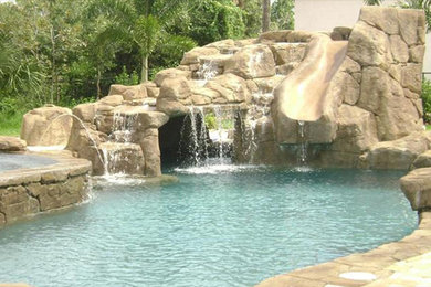 Diseño de piscina con tobogán natural a medida en patio trasero con adoquines de hormigón