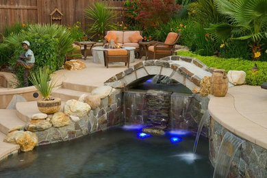 Ejemplo de piscina con fuente clásica renovada grande a medida en patio trasero con adoquines de hormigón