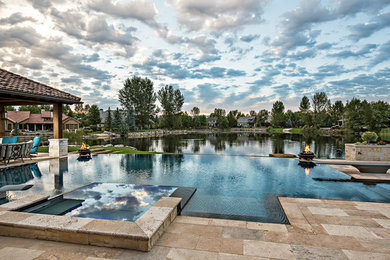 Inspiration for a large mediterranean back custom shaped infinity hot tub in Boise with natural stone paving.