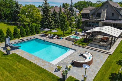 Ejemplo de piscina con tobogán clásica grande rectangular en patio trasero con adoquines de piedra natural