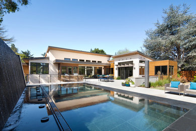 Ejemplo de piscina con fuente infinita actual de tamaño medio rectangular en patio trasero con adoquines de piedra natural