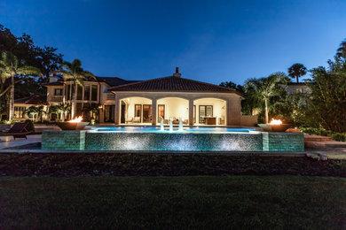Immagine di una grande piscina mediterranea personalizzata dietro casa con fontane e pavimentazioni in pietra naturale