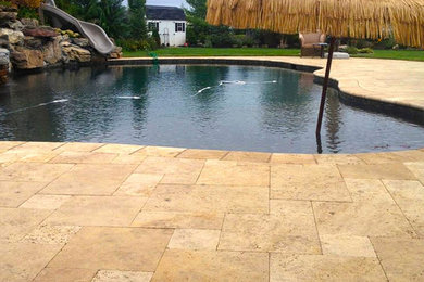 Modelo de piscina con tobogán mediterránea grande a medida en patio trasero con adoquines de piedra natural