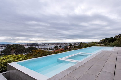 Diseño de piscina infinita contemporánea grande rectangular en patio trasero con adoquines de hormigón