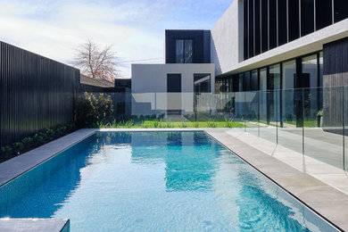 Imagen de piscina alargada moderna de tamaño medio rectangular en patio trasero con paisajismo de piscina y suelo de baldosas
