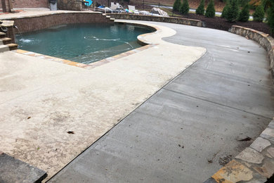 Modelo de piscina con fuente elevada minimalista grande a medida en patio trasero con suelo de hormigón estampado