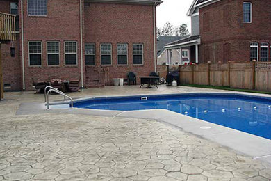 Modelo de piscina de tamaño medio rectangular en patio trasero con suelo de hormigón estampado