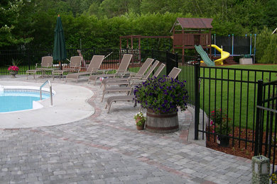 This is an example of a back custom shaped swimming pool in Boston with a water feature and concrete paving.