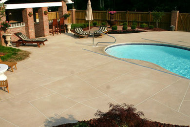Photo of a large classic back kidney-shaped lengths swimming pool in Cincinnati with a pool house and stamped concrete.