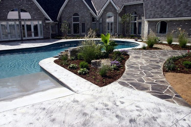 This is an example of a large traditional back custom shaped lengths swimming pool in Cincinnati with a water feature and stamped concrete.