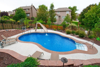 Ejemplo de piscina con tobogán clásica grande tipo riñón en patio trasero con adoquines de hormigón