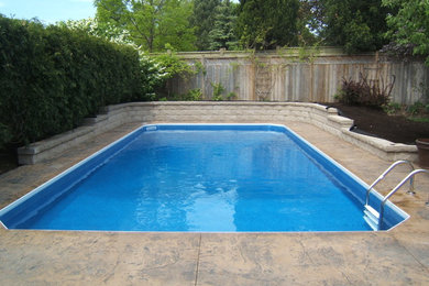 Modelo de piscina alargada tradicional de tamaño medio rectangular en patio trasero con losas de hormigón