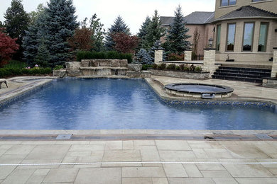 Inspiration för en stor amerikansk l-formad pool på baksidan av huset, med en fontän och naturstensplattor