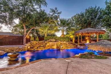 Inspiration for a tropical backyard stamped concrete and custom-shaped pool fountain remodel in Dallas