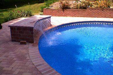 Modelo de piscina con fuente tradicional grande redondeada en patio trasero con suelo de baldosas