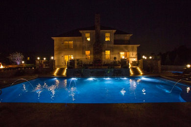 Diseño de piscina con fuente alargada tradicional grande rectangular en patio trasero con losas de hormigón