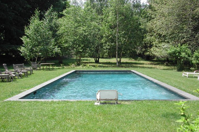 Modelo de piscina alargada actual de tamaño medio rectangular en patio trasero con losas de hormigón