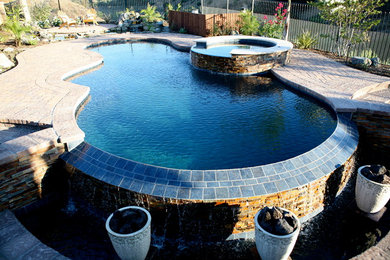 Photo of a large classic back custom shaped infinity hot tub in Los Angeles with natural stone paving.